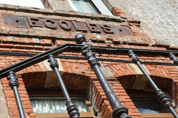 Batiment d'une vieille école pour filles et pour garçons. L'enseigne est toute rouillée, vintage, sur un vieux mur en briques rouges.