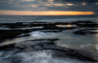 Sunset on a rocky coast with dramatic cloudy sky.