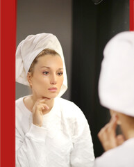 woman looking in the mirror in the bathroom and taking care of her skin.