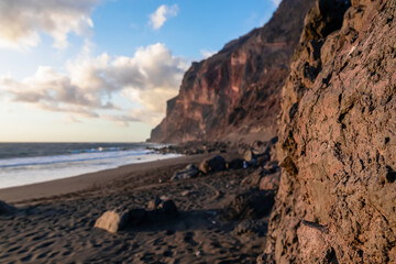 Fototapeta na wymiar Scenic view during sunset on the volcanic sand beach Playa del Ingles in Valle Gran Rey, La Gomera, Canary Islands, Spain, Europe. Massive cliffs of the La Mercia range. Close up on Rock formation