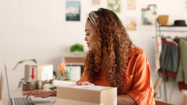 Delivery, online order and woman in fashion on laptop while working at a boutique. Young, happy and African designer shipping stock of clothes in boxes and pc for service at a small business