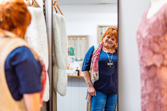 Happy middle aged woman looking in mirror in plus sized clothing boutique