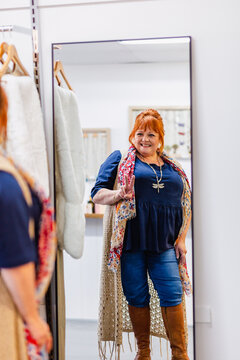 Happy middle aged woman looking in mirror in plus sized clothing boutique