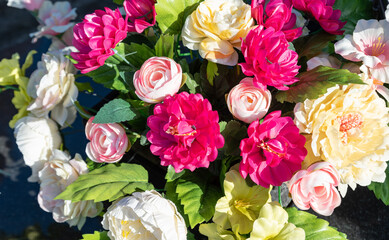 Bunches of artificial flowers in close-up. Faded artificial flowers on the grave. Colorful flowers on the grave.