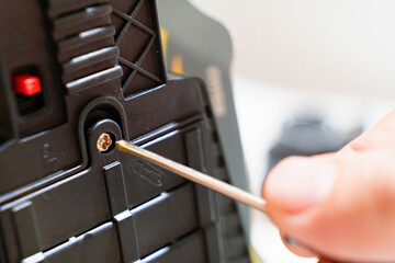 A person with a screwdriver opens the compartment for batteries and accumulators in the device. replacement and charging of batteries.