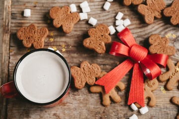 gingerbread man, cocoa and cookies with a big red bow on a wooden background, top view. Various christmas sweets with a cup of cocoa on the table