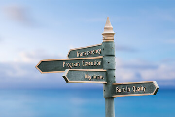 transparency program execution alignment built in quality four word quote written on fancy steel signpost outdoors by the sea.