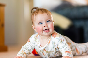 happy five month old baby girl with blue eyes learning to crawl on floor