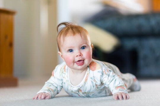 Happy baby girl learning to crawl doing tummy time on living room floor