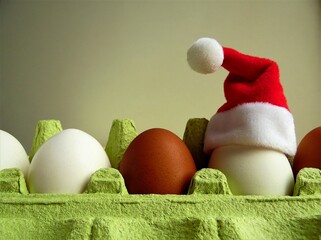 Santa's hat on an egg, white and brown eggs in a tray and Santa's hat on one of the eggs, Christmas theme
