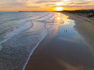Aerial view of gentle waves on a beach with reflection of a sunset