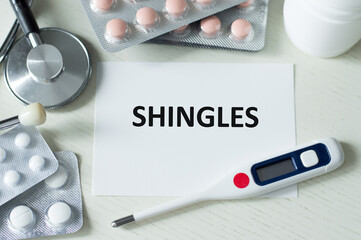 Word SHINGLES text on a card on a table next to a stethoscope, thermometer and tablet on the table