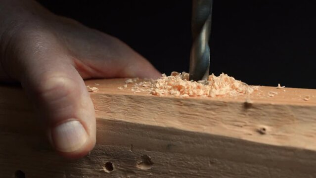 Slow motion close up of drill bit drilling into wood. Joinery and construction work close up. Wood chippings fly off a metal drill. Handyman bores holes into a wooden board. 