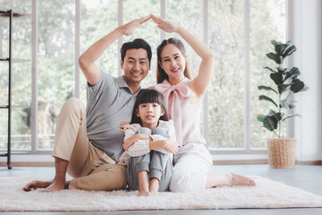 Happy young asian family father mother making hands shape house roof with little cute daughter at home. Family relocation or insurance protecting concept