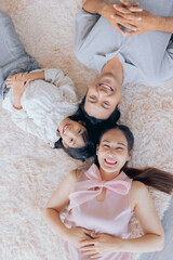 Obraz na płótnie Canvas Young asian parents and cute small kids girl smiling laughing lying on carpet together, happy family bonding fun enjoy lovely moments in living room at home, top view