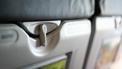 Close-up at part of table tray's securing pin on backrest of airplane passenger seat. Transportation vehicle equipment object, selective focus.