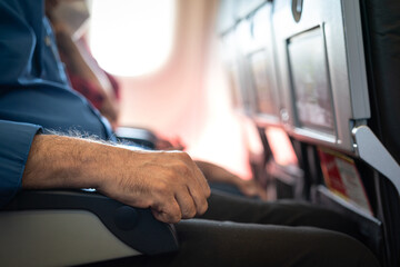Hand of a airplane passenger is placed on an armrest during sitting at the economy class seat row....