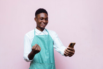 cheerful young handsome african cook jubilating holding and looking at a smartphone in hand