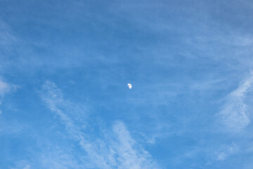 The waning moon, daytime on the blue sky, among the clouds