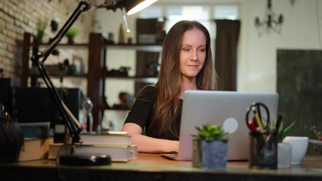 Young female entrepreneur working sitting at a desk typing on laptop computer in home office. Portrait of happy smiling caucasian woman at home.
