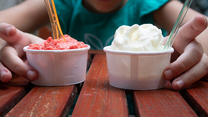 Child with two paper cups of ice cream. Close-up of a hand holding a treat