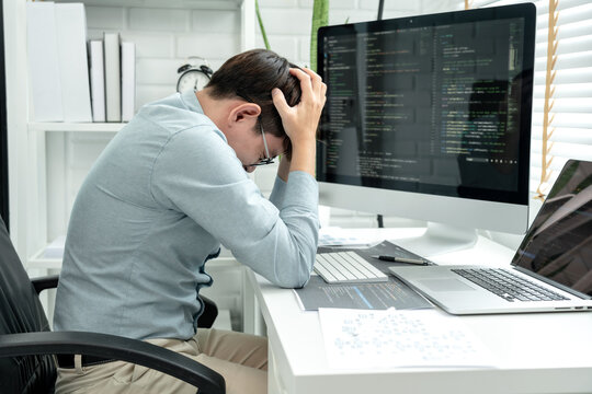 Male programmer feeling headache and stress during checking program code and debugging on multiple screens