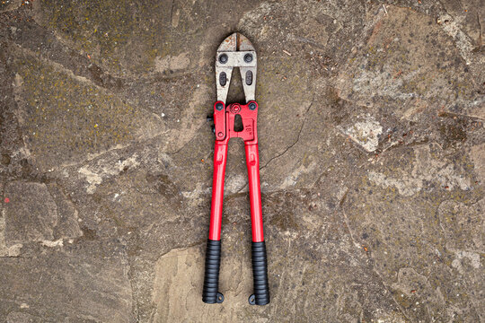 Bolt cutter with red handles on the stone surface.