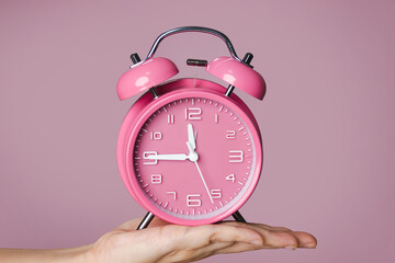 Woman hand hold pink alarm clock which set at fifteen before twelve. Start new business target,...