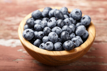 Blueberry berries are in a wooden plate on wooden background. Healthy food and healthy lifestyle.