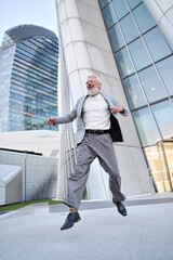 Happy cool successful stylish old senior professional business man wearing suit jumping outdoors in big city business office district feeling free winner celebrating financial freedom and leadership.