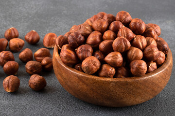 Top view of a bowl full of hazelnuts on dark background
