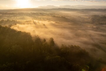 Aerial colorful view of foggy autumn morning over hills and forests, in Soceni village, Romania. Captured from above, with a drone.