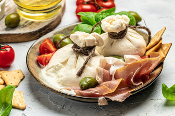 Antipasto burrata cheese salad served with cherry tomatoes, fresh basil leaves, prosciutto ham and olives. prosciutto, mozzarella. top view. place for text