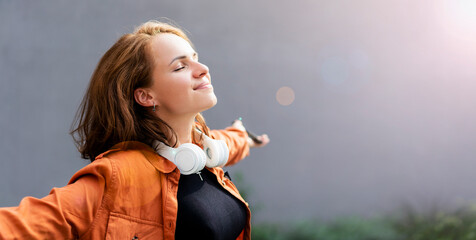 Joyful and satisfied woman with closed eyes in casual clothes and big headphones on her neck,...