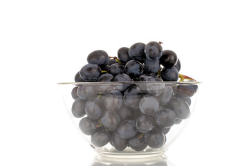 One sprig of sweet black grapes in a glass dish, macro, isolated on white background.