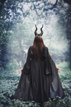 witch in a black cloak with horns Maleficent in the forest, in the fog, back view