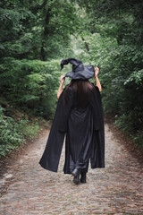 A witch in a black cloak with hat in a dark forest