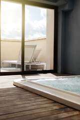 Jacuzzi room at the back of the room with glass and view of the terrace with deckchairs.