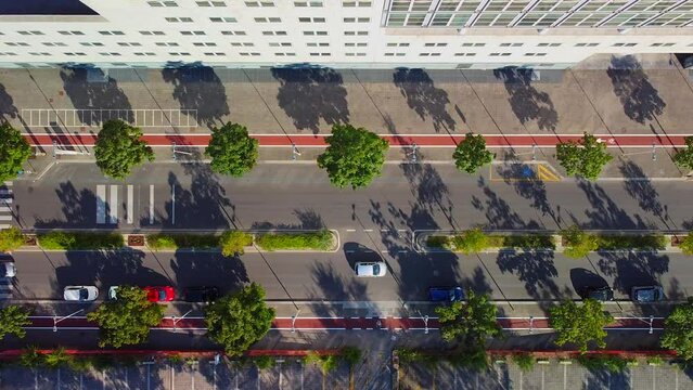Top view of cars. Car traffic in the urban part of the city is lively. The drone flies from top to bottom, shooting at parked cars right along the street. Trees by the road. Zebra. Sidewalk 