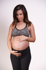Thoughtful beautiful 30s-40s pregnant woman exercising and touching belly 