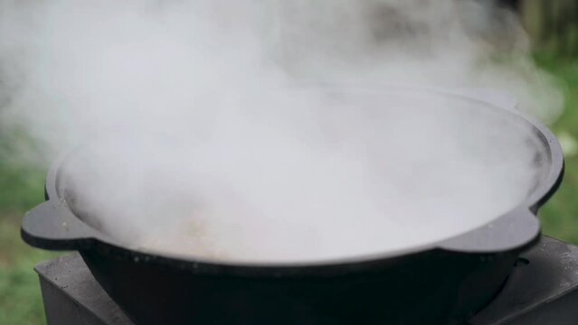 The cook covers the prepared gravy for pilaf in a cast-iron cauldron. Close-up.