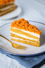 Carrot cake with cream cheese in layers and carrots on top on a  blue and white background with carrots in blurry background