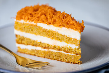 Carrot cake with cream cheese in layers and carrots on top on a  blue and white background with carrots in blurry background