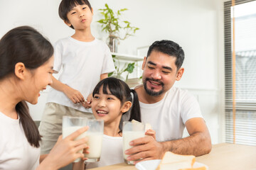 Asian  family enjoying breakfast at living room. little girl daughter sitting on table, drinking milk with smiling father and mother in morning. Happy family at home.
