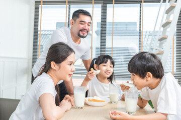 Asian  family enjoying breakfast at living room. little girl daughter sitting on table, drinking milk with smiling father and mother in morning. Happy family at home.