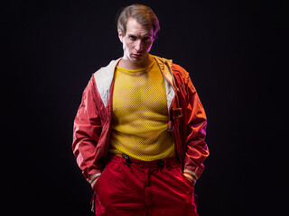 a young muscular man in a bright outfit poses in a pretentious pose, style and grotesque. Attractive guy with pumped-up arms in a mesh T-shirt and red pants, photo in smoke - obrazy, fototapety, plakaty
