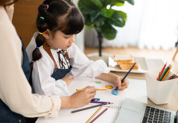 Happy asian mother and daughter having video call, waving and smiling at laptop screen, sitting in kitchen .School girl using computer, having online lesson while coronavirus pandemic.