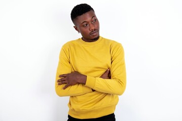 Displeased young handsome man wearing yellow sweater over white background with bad attitude, arms crossed looking sideways. Negative human emotion facial expression feelings.