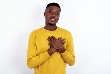 Honest young handsome man wearing yellow sweater over white background keeps hands on chest,...