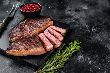 Grilled top sirloin or cup rump beef meat steak on marble board. Black background. Top view. Copy...